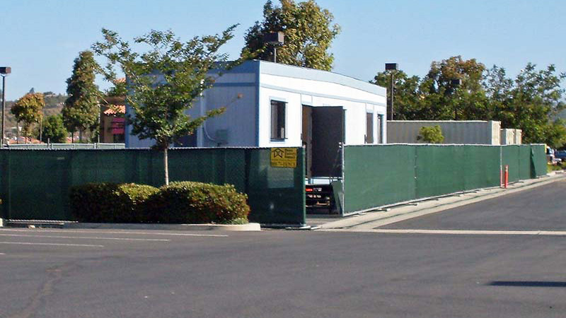 Portable fence panels near Biola, California, with green privacy screen surrounding a construction office.