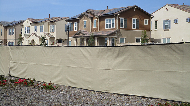 Armona construction fence rentals with beige privacy screen in front of a group of houses.
