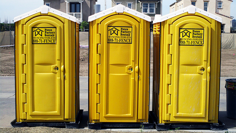 Three yellow porta potties with houses in the background, some of our portable bathrooms for rent near Armona, California.