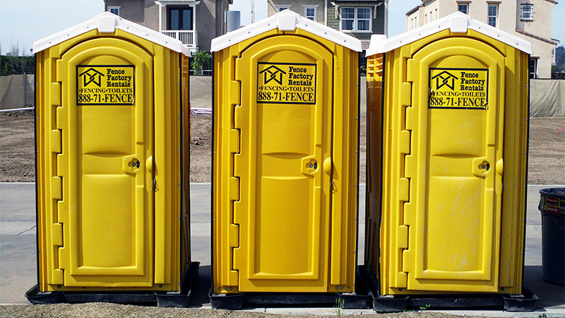 Three yellow porta potties with houses in the background, some of our portable bathrooms for rent near Atascadero, California.