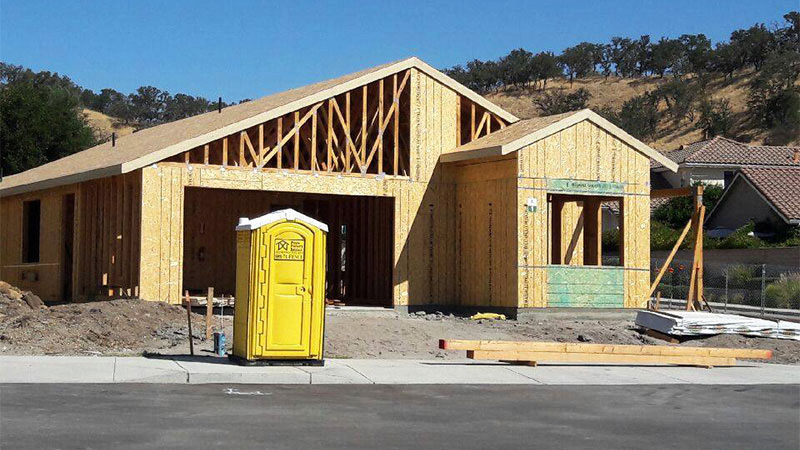 Kerman portable restroom rental in front of house construction.