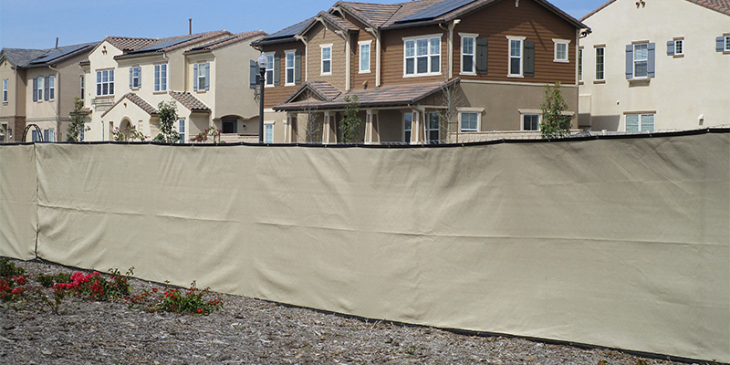 Commercial temporary fencing near Madera, California with beige privacy screen in a housing community.